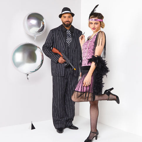 Man and woman wearing 1920s costumes beside silver party balloons.